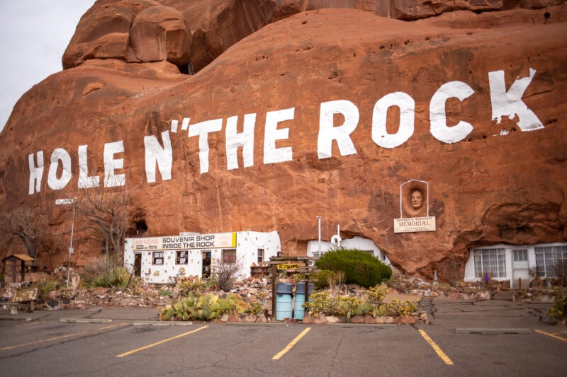 a red rock formation painted with the white words "hole n" the rock" with a parking lot and gift shop