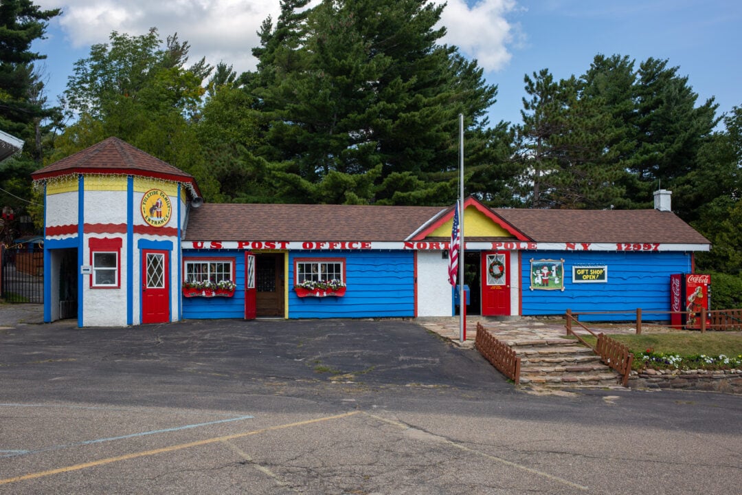 a small wood-sided post office building painted red white blue and yellow with the words "us post office north pole ny" painted on top