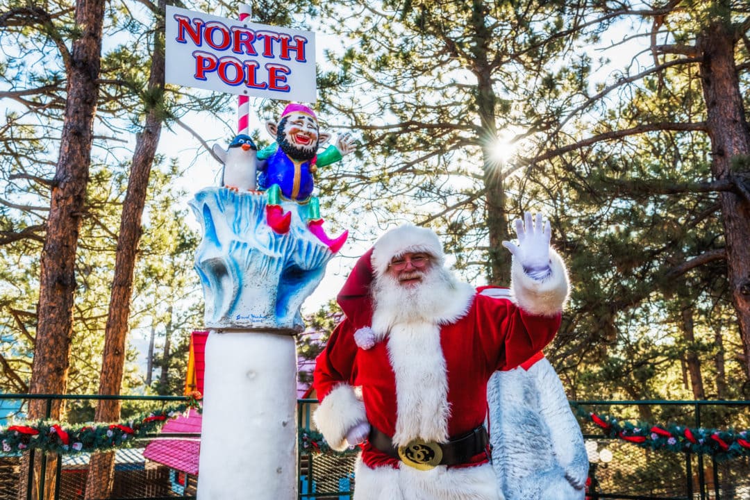 santa smiles and waves next to a sign for the north pole