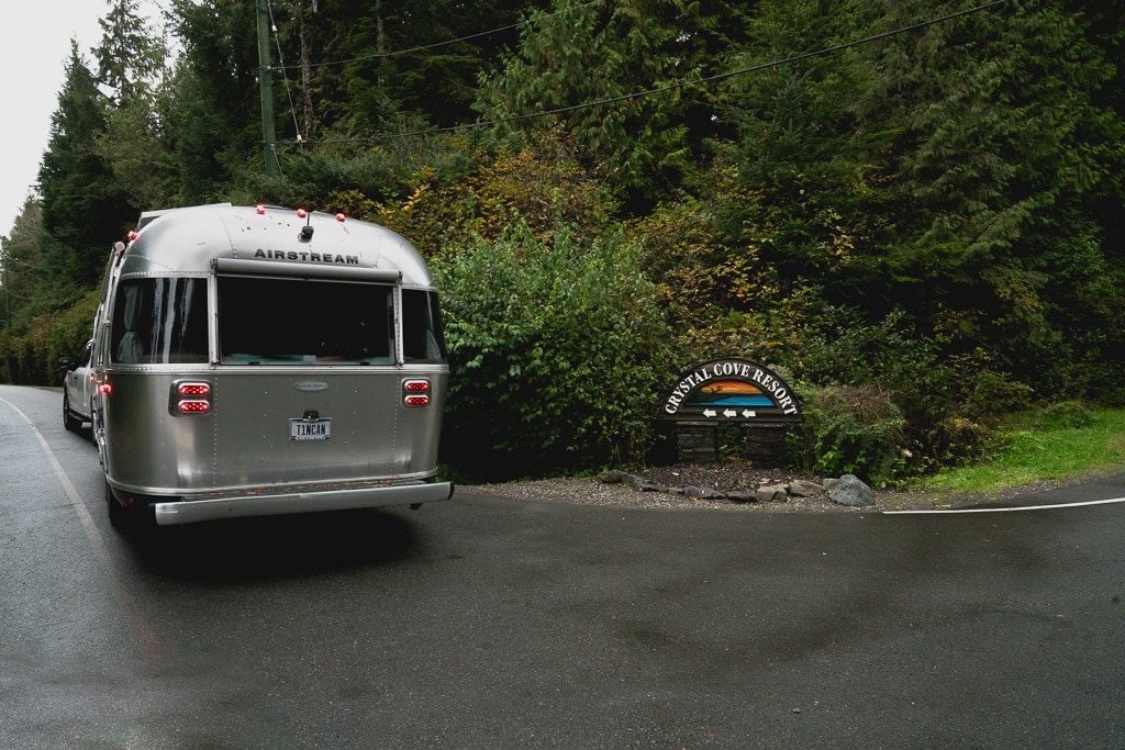 a silver airstream trailer parked next to a campground entrance with a wooden sign that says "crystal cove resort"