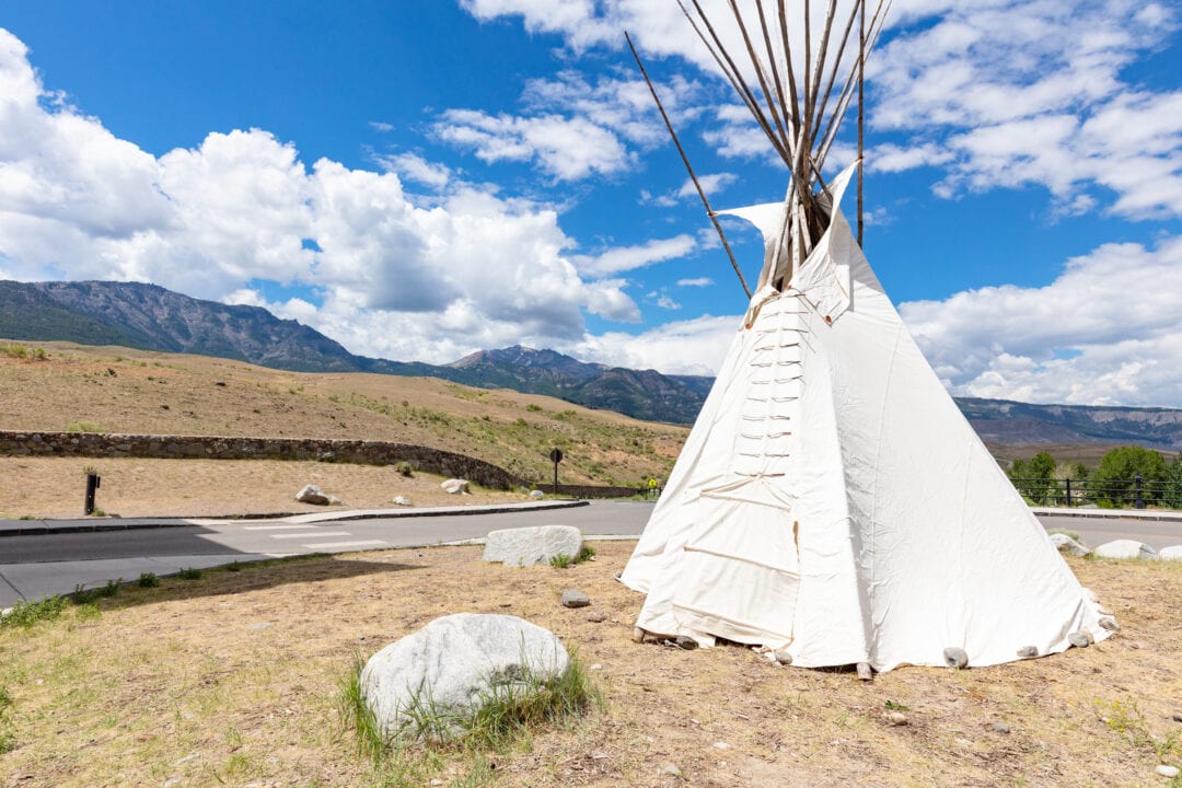 a white teepee is near a road and in front of a blue sky with clouds